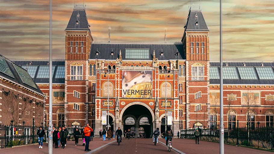 Peatones y ciclistas se mueven por un camino compartido frente a un edificio histórico en Ámsterdam.