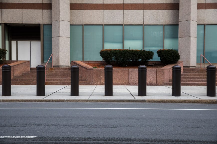 Row of black bollards installed along a sidewalk in front of a commercial building