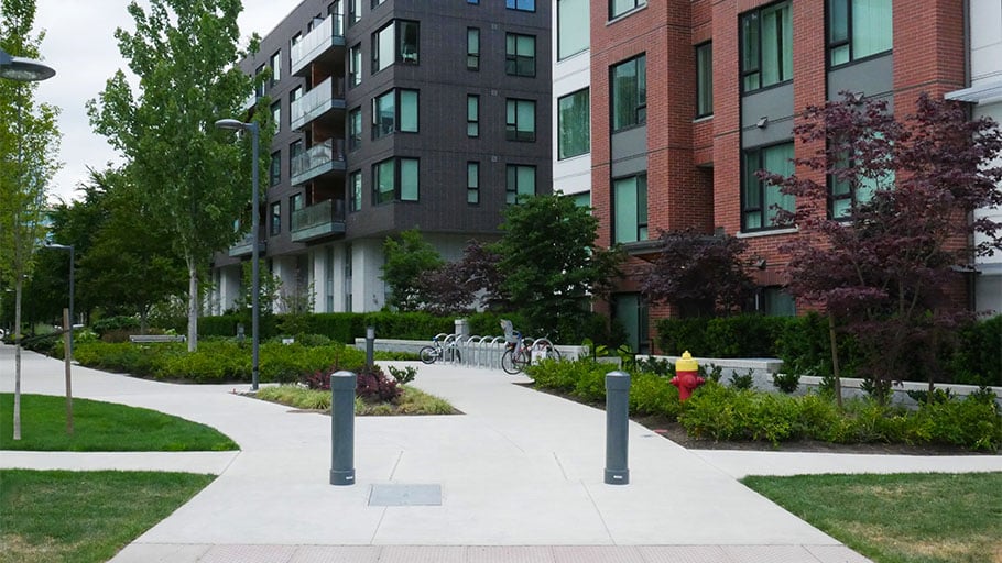 Two security bollards stand along a residential pathway, balancing pedestrian flow with vehicle access control.