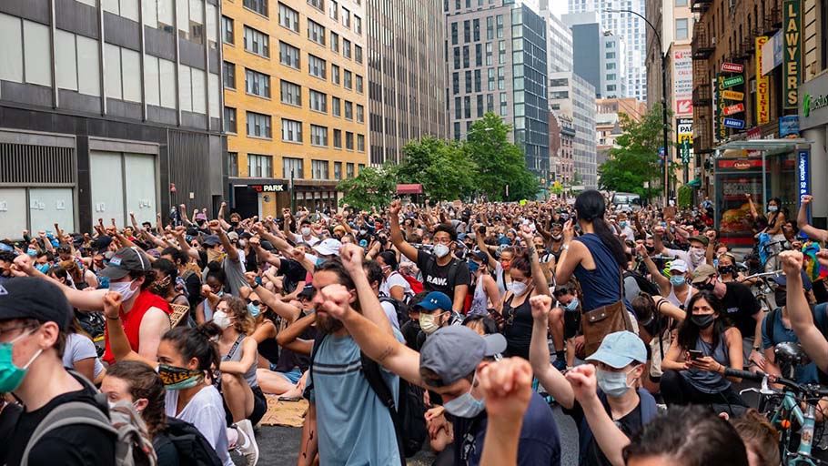 A large crowd of demonstrators raise their fists in solidarity during a peaceful protest in a city street.