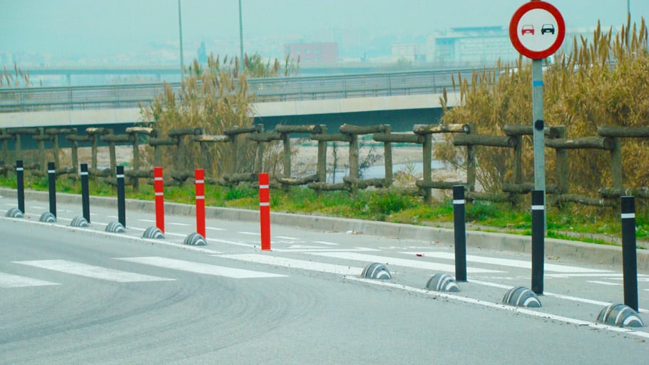 A road section with traffic control bollards and signage directing vehicle movement.
