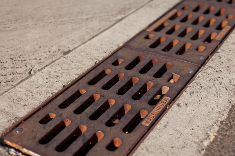 A red-brown trench grate is installed in a municipal sidewalk