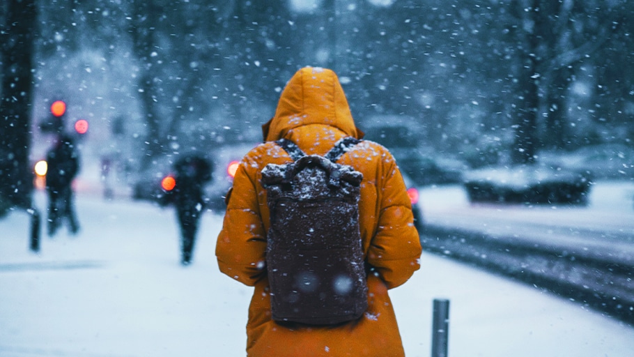 A pedestrian in a yellow jacket walks along a snowy sidewalk