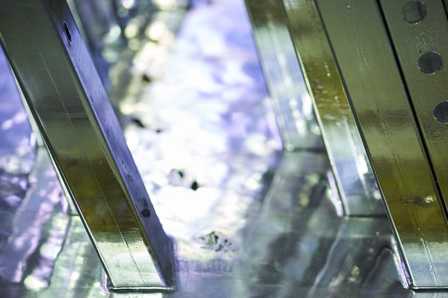 Square hollow rods are pulled shining out of a bath of silvery liquid during hot-dip galvanization