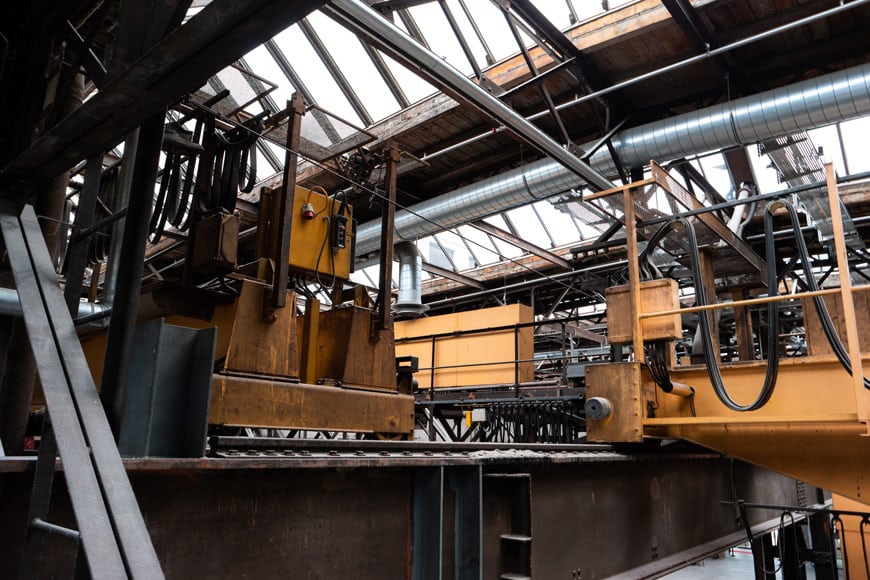 A heavy yellow machine sits atop a platform with raised rails in an abandoned factory.