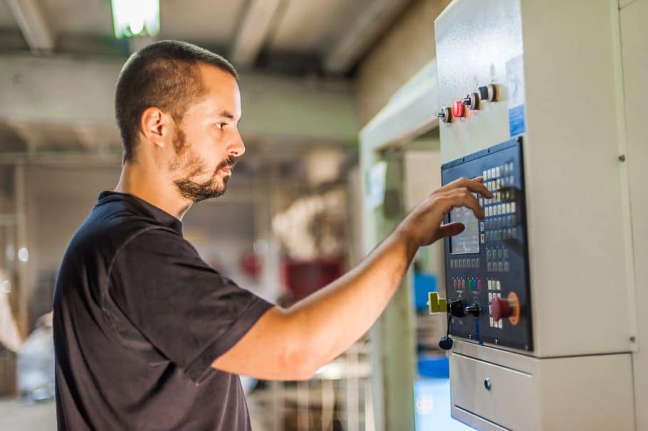 A machinist works a factory control panel