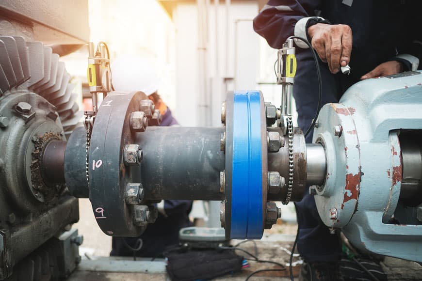 A millwright inspects the alignment of a pump and motor