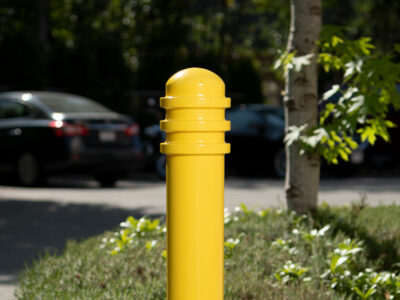 A bright yellow bollard is highly visible in a parking lot full of cars