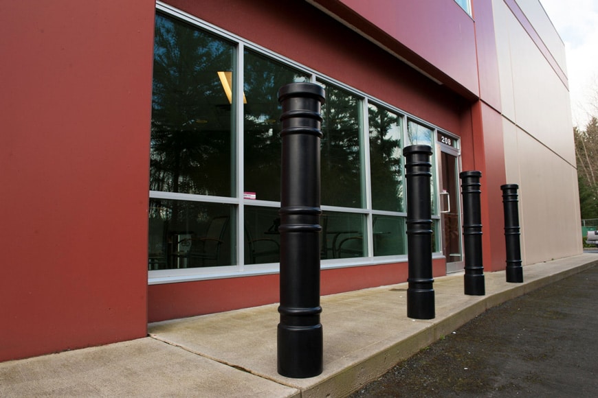 Four slender black bollards with three sets of decorative rings protect office building