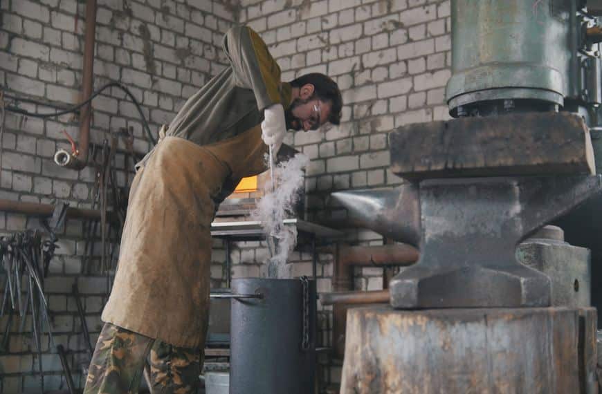 A bladesmith wearing safety clothing oil quenches his work before tempering it.