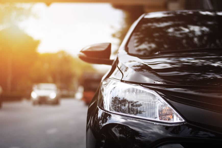Close up picture of headlight of shiny black car parked on the street at sunset