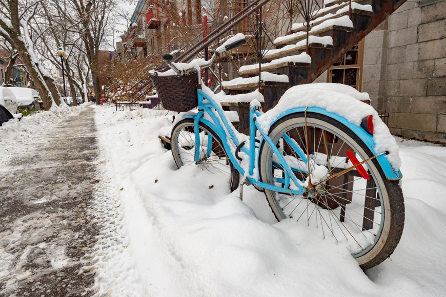 A blue bicycle covered in snow is parked at an outdoor bike rack